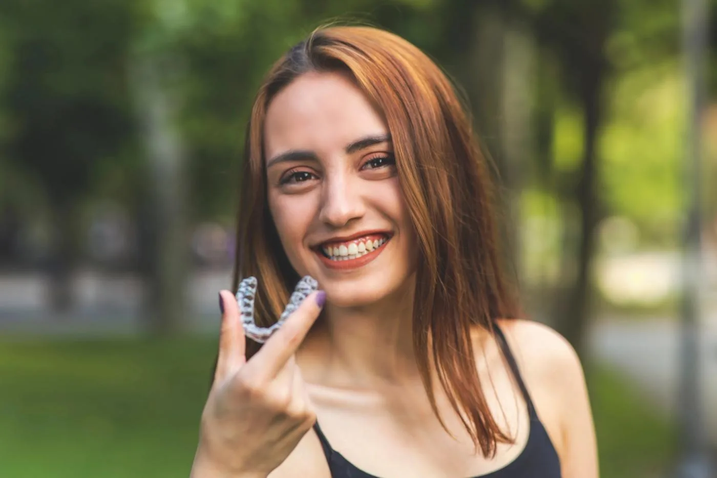 A smiling patient holding a clear aligner